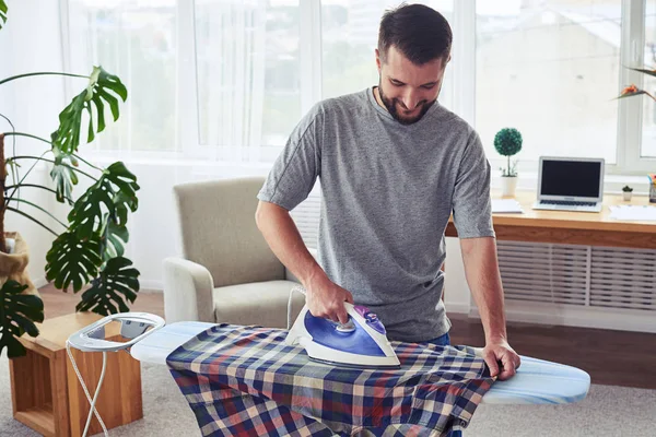 Man with charming smile ironing diligently shirt on board — Stock Photo, Image