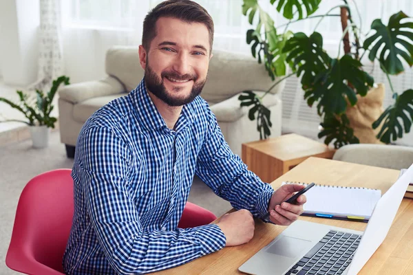 Homme souriant assis à table et tenant le téléphone — Photo