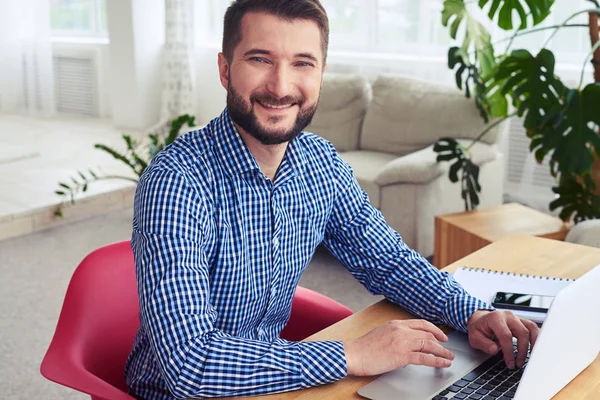 Businessman with nice smile sitting at table and working with la