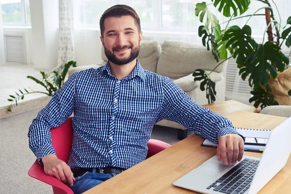 Encantador marido sentado à mesa e trabalhando com laptop — Fotografia de Stock