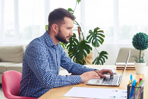 Konzentrierter Herr im blau karierten Hemd, der mit Laptop arbeitet — Stockfoto