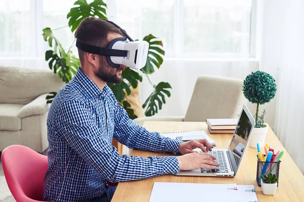 Man in VR glasses working with laptop sitting at table — Stock Photo, Image