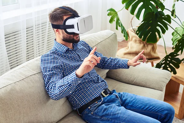 Guy in blue shirt using virtual reality glasses sitting on sofa — Stock Photo, Image