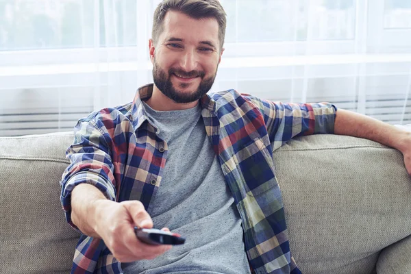 Hombre sonriente en canal de cambio de camisa a cuadros con control remoto —  Fotos de Stock