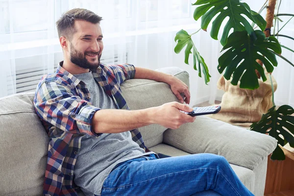 Glad kille med skägg byter kanal med fjärrkontroll — Stockfoto