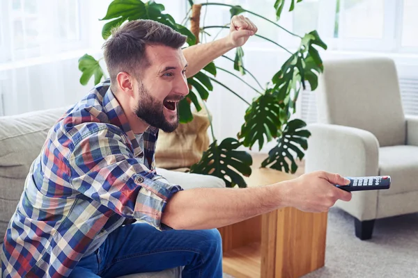 Homem atraente torcendo e comutando canal com contro remoto — Fotografia de Stock