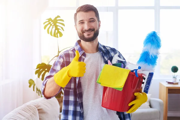 Cheerful bachelor holding cleaning set ant putting thumb up — Stock Photo, Image
