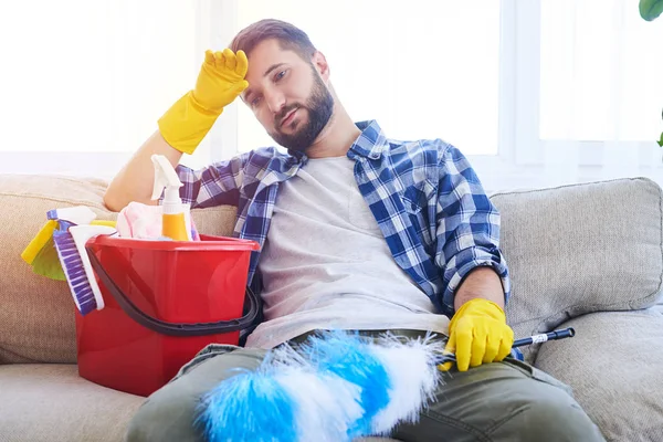 Senhor exausto sentado no sofá com conjunto de limpeza — Fotografia de Stock