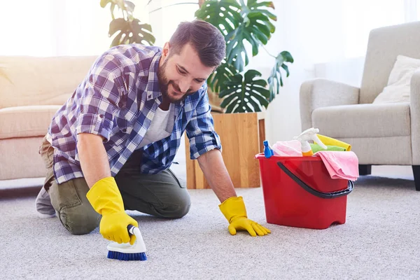 Nice male in gloves brushing carpet — Stock Photo, Image