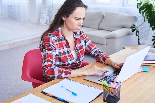 Ernsthafte Frau arbeitet im Laptop, während sie am Schreibtisch sitzt — Stockfoto