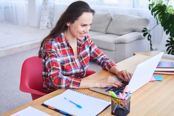 Усміхнена жінка працює в ноутбуці, сидячи за столом — стокове фото
