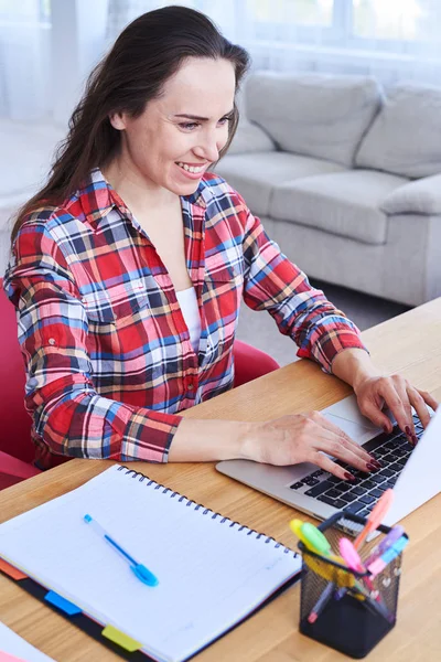 Chica encantadora que trabaja en el ordenador portátil mientras está sentado en el escritorio —  Fotos de Stock