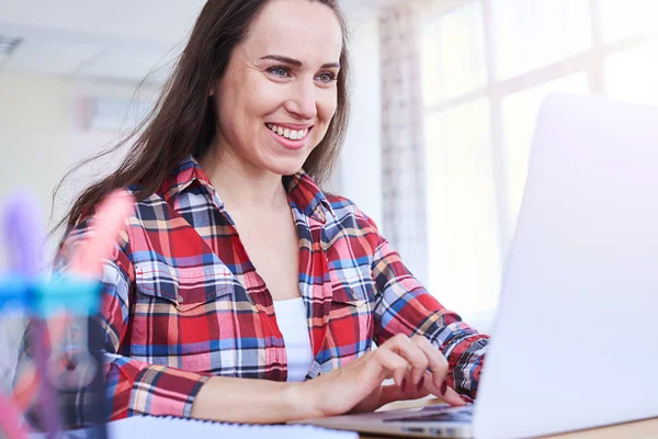 Zufriedene Dame arbeitet im Laptop, während sie am Schreibtisch sitzt — Stockfoto