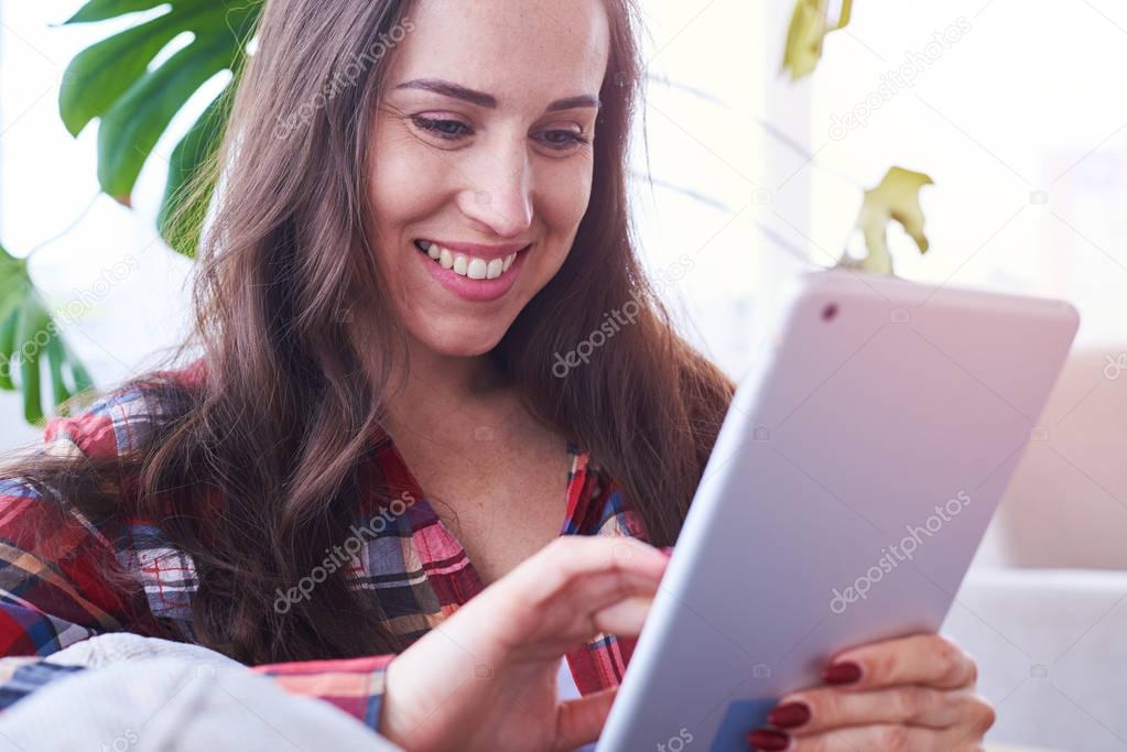 Appealing girl surfing in tablet while sitting on sofa