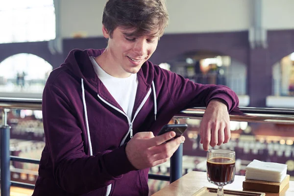 Stijlvolle jongen surfen in mobiele telefoon zitten over kopje koffie — Stockfoto