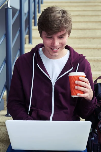 Delightful man holding cup of coffee and chatting in laptop — Stock Photo, Image