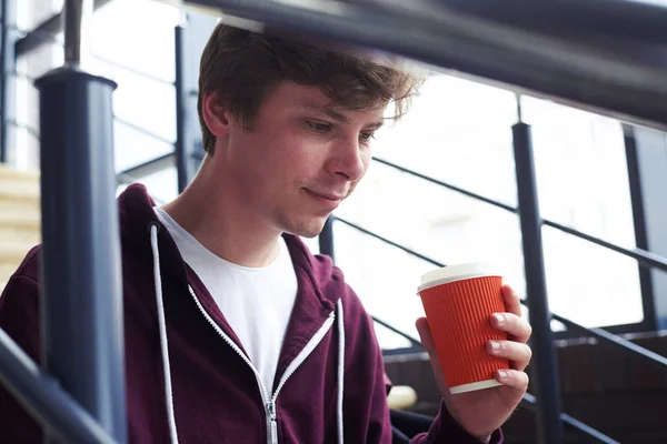 Bello ragazzo che tiene in mano una tazza di caffè e lavora nel computer portatile — Foto Stock