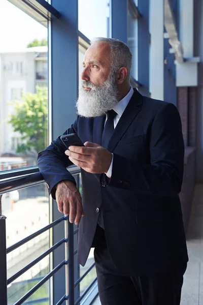 Good-looking man looking out window while surfing in mobile phon — Stock Photo, Image