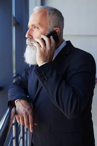 Hombre barbudo hablando por teléfono mientras mira por la ventana —  Fotos de Stock