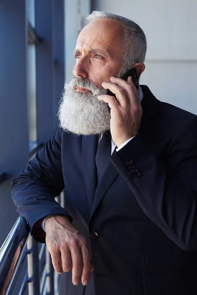 Senhor severo falando ao telefone enquanto olha pela janela — Fotografia de Stock