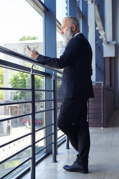 Humorless male with gray beard surfing in phone — Stock Photo, Image