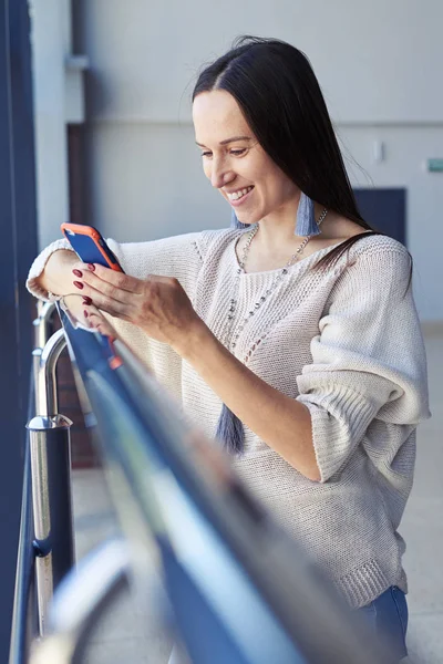 Glad flicka surfing i telefonen medan lutande på ledstången — Stockfoto