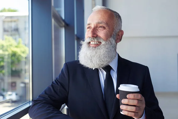 Trevlig man leende medan du håller kaffe och tittar ut fönstret — Stockfoto