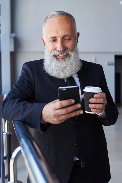 Гарний бородатий сер тримає чашку кави та серфінгу в телефоні — стокове фото