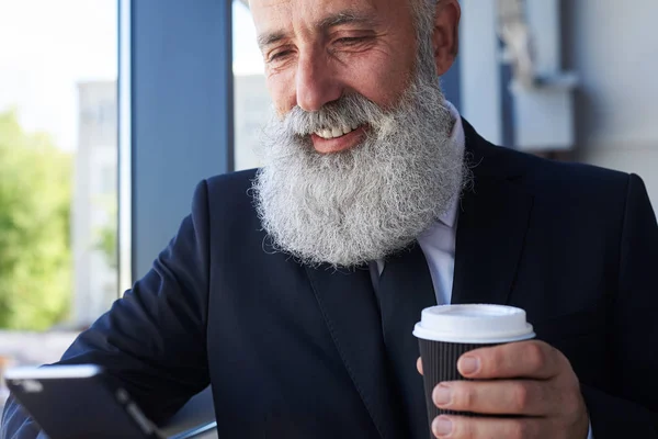 Joyful idade masculina de 50-60 segurando xícara de café e surf em ph — Fotografia de Stock