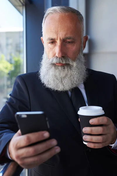 Triste senhor idade de 50-60 segurando xícara de café e surf no telefone — Fotografia de Stock