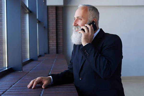 Encantador señor hablando por teléfono mientras se apoya en el alféizar —  Fotos de Stock