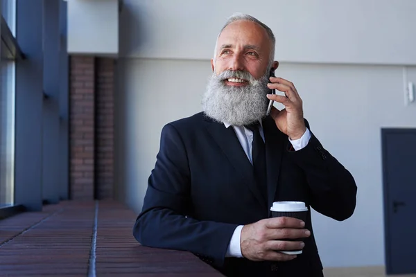 Hombre guapo con barba gris hablando por teléfono mientras sostiene la taza —  Fotos de Stock