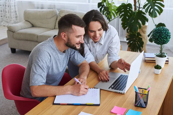 Husband writing in notebook while wife showing something to him — Stock Photo, Image