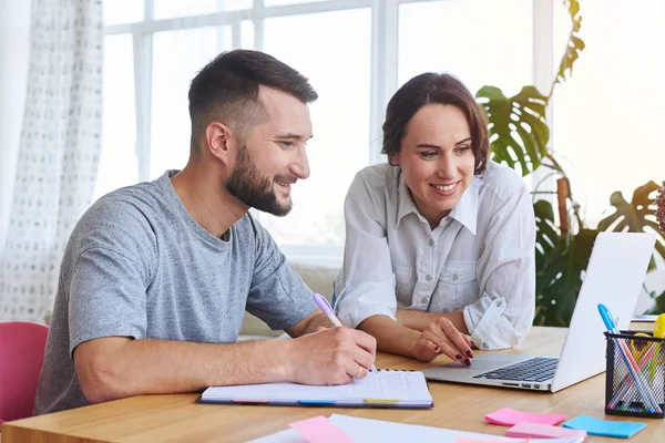 Bearded guy writing in notebook while girl surfing in Internet — Stock Photo, Image