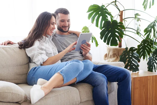 Leende par sitter på soffan och surfing i tablett — Stockfoto