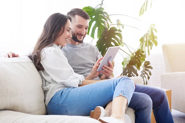 Schönes Paar sitzt auf dem Sofa und surft im Tablet — Stockfoto