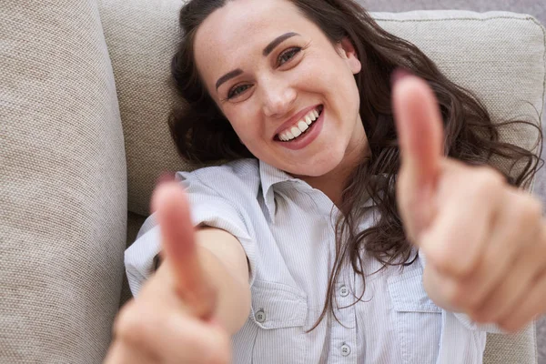 Wonderful brunet showing thumb up and lying on sofa — Stock Photo, Image