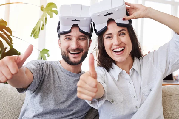 Усміхнена пара в VR окулярах показує великі пальці вгору — стокове фото