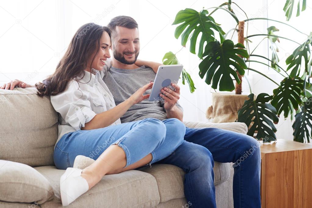 Smiling couple sitting on sofa and surfing in tablet