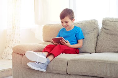 Küçük çocuk tablet ile kanepede otururken yan görünüm