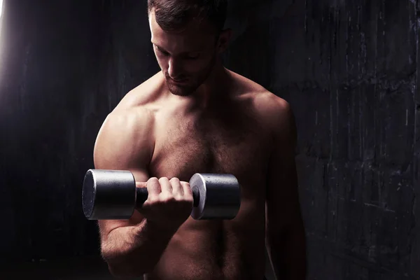 Knappe bodybuilder poseren shirtless met halter in schemerig licht — Stockfoto
