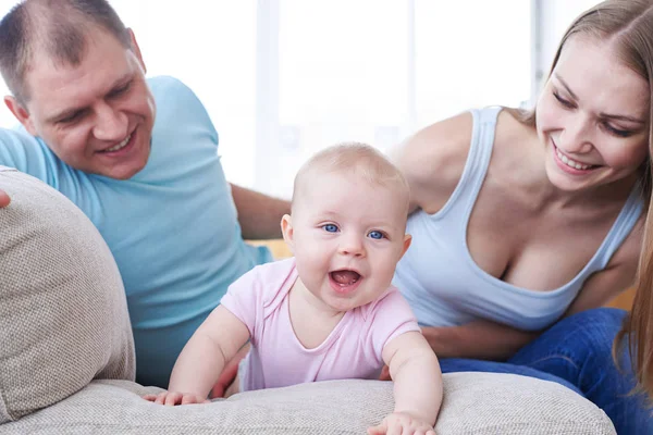 Fröhliches Kind krabbelt auf Sofa und glückliche Eltern schauen es sich an — Stockfoto