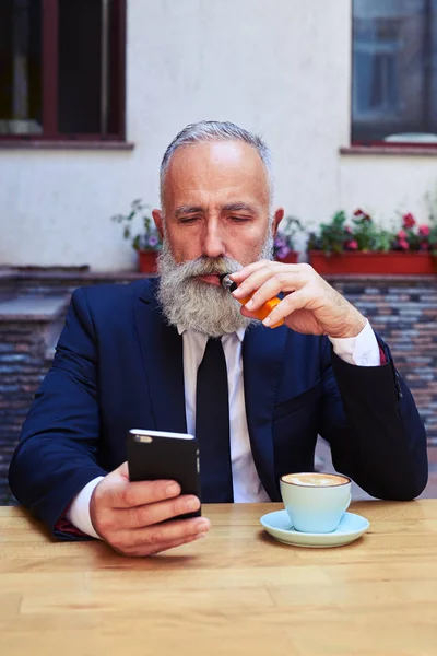 Um homem idoso barbudo olhando para o smartphone — Fotografia de Stock