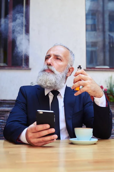 Ernstige man electrocigarette roken en surfen in telefoon — Stockfoto