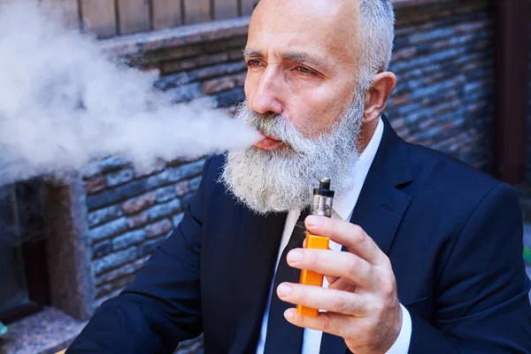 Apuesto señor exhalando humo mientras fuma electrocigarrillo — Foto de Stock