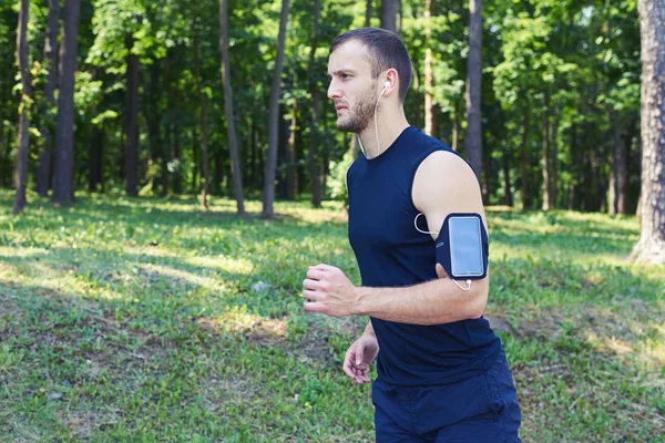 Sportieve man loopt in park terwijl u luistert naar muziek — Stockfoto