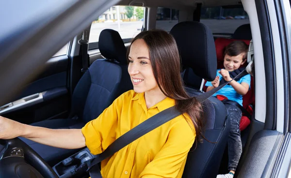 Hezká žena řidičské auto s syn sedí v dětské autosedačky — Stock fotografie