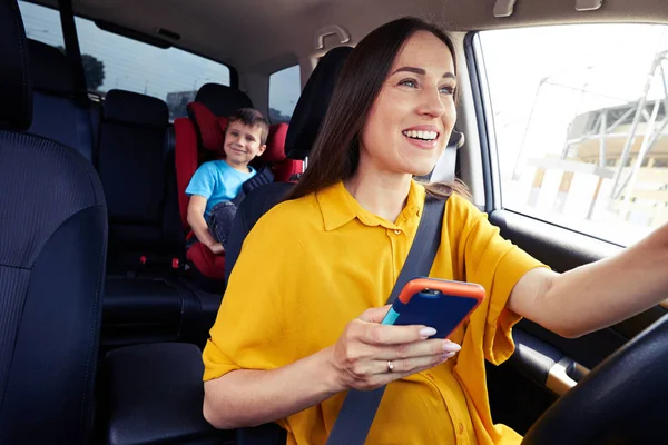 Sorrindo mãe dirigindo um carro, segurando telefone — Fotografia de Stock