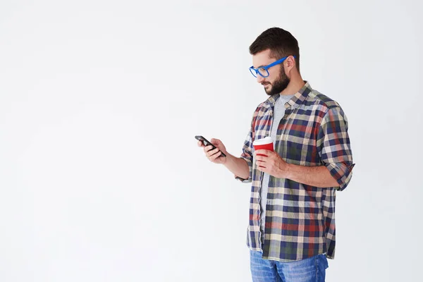 Cheerful bearded man standing with cup of coffee and smartphone — Stock Photo, Image