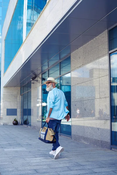 Bonito senhor andando rua abaixo enquanto carrega bolsa — Fotografia de Stock